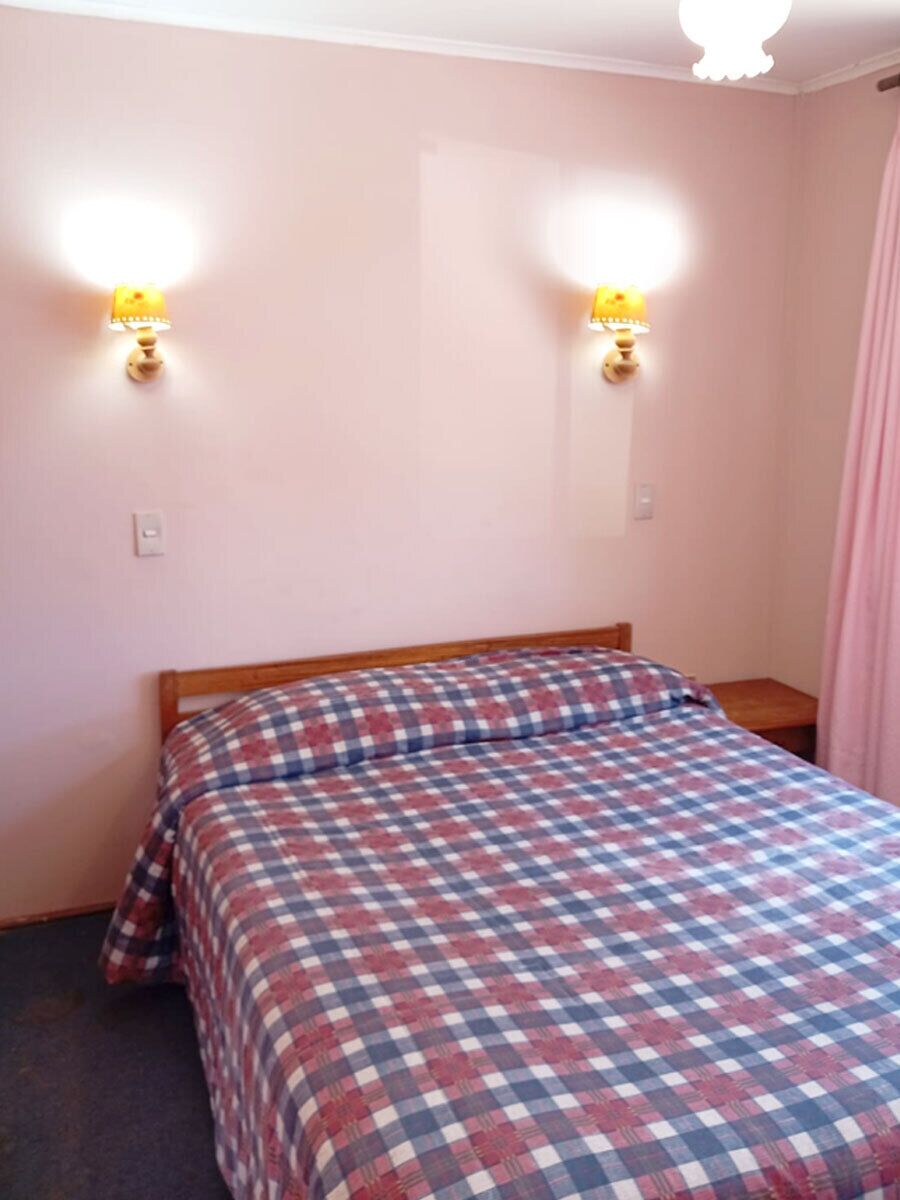 A single bed with a checkered bedspread, two wall-mounted lamps, and a wooden headboard.