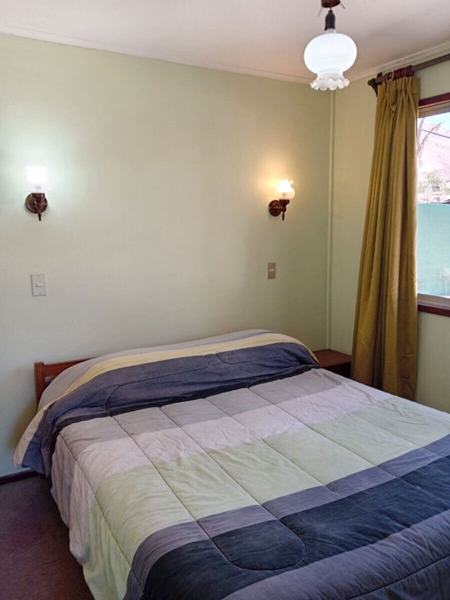 Un dormitorio con cama, dos lámparas de pared, una ventana con cortinas e iluminación en el techo.