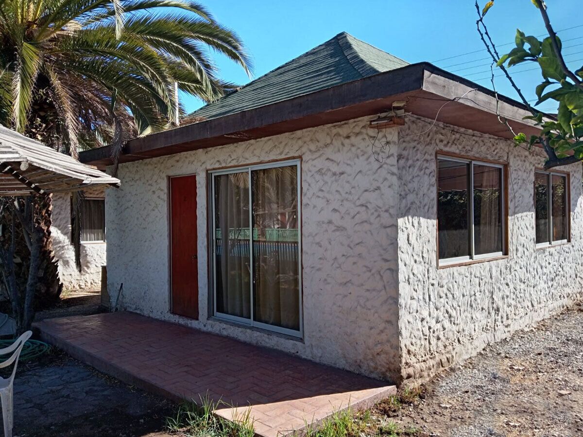 Una casa de un solo piso con puerta roja, amplios ventanales correderas y un pequeño porche.