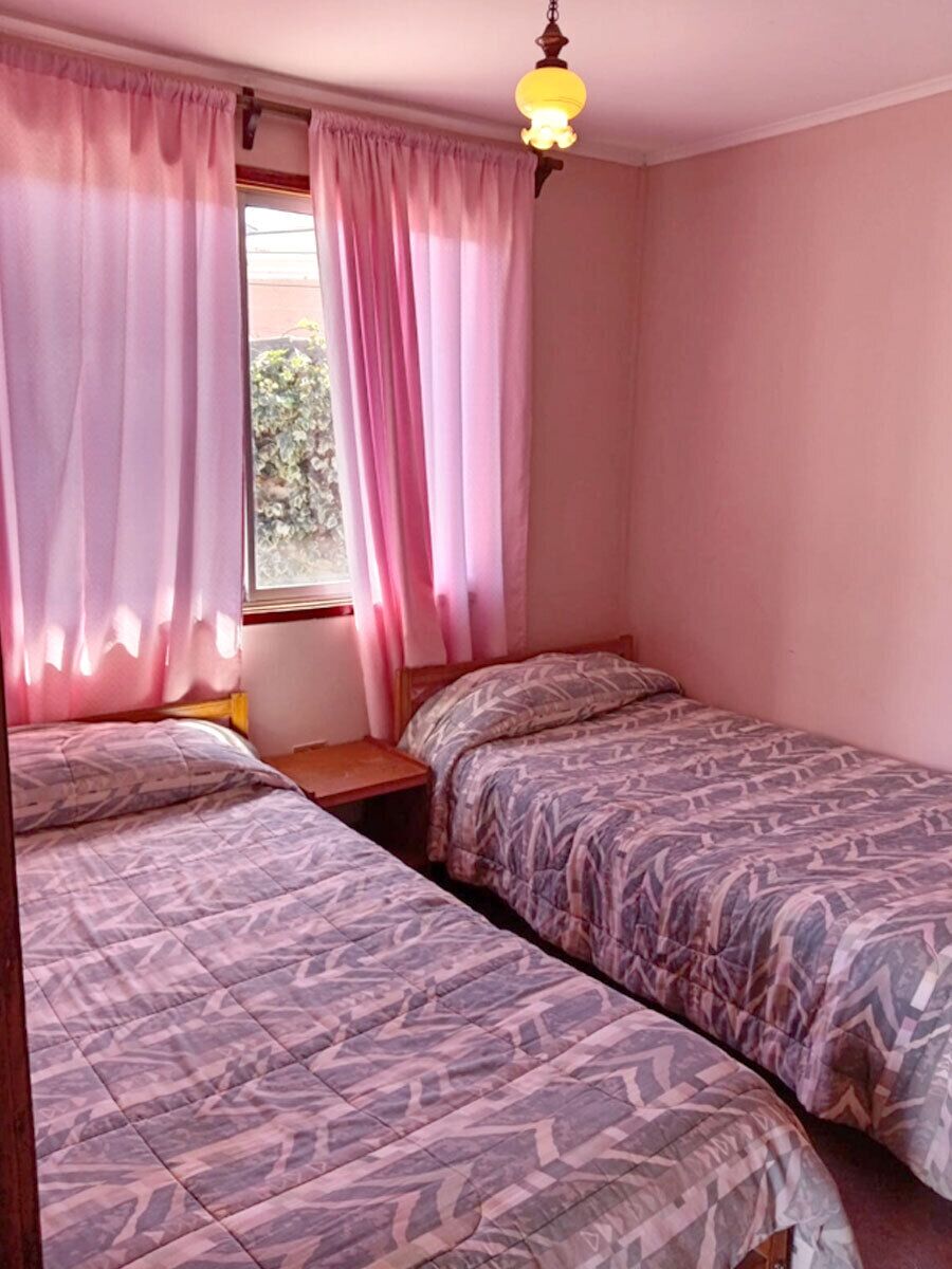 Ein Schlafzimmer mit zwei Betten, einem Fenster mit Vorhängen und einer Deckenleuchte.