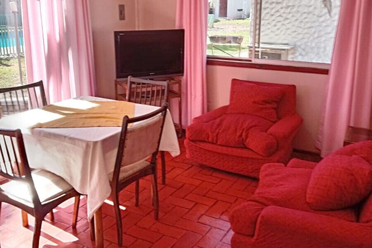 A room with a dining table, chairs, a TV, and a red sofa.
