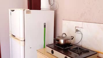 A compact kitchen with a white refrigerator, a wooden cabinet, a gas stove, and a small window.