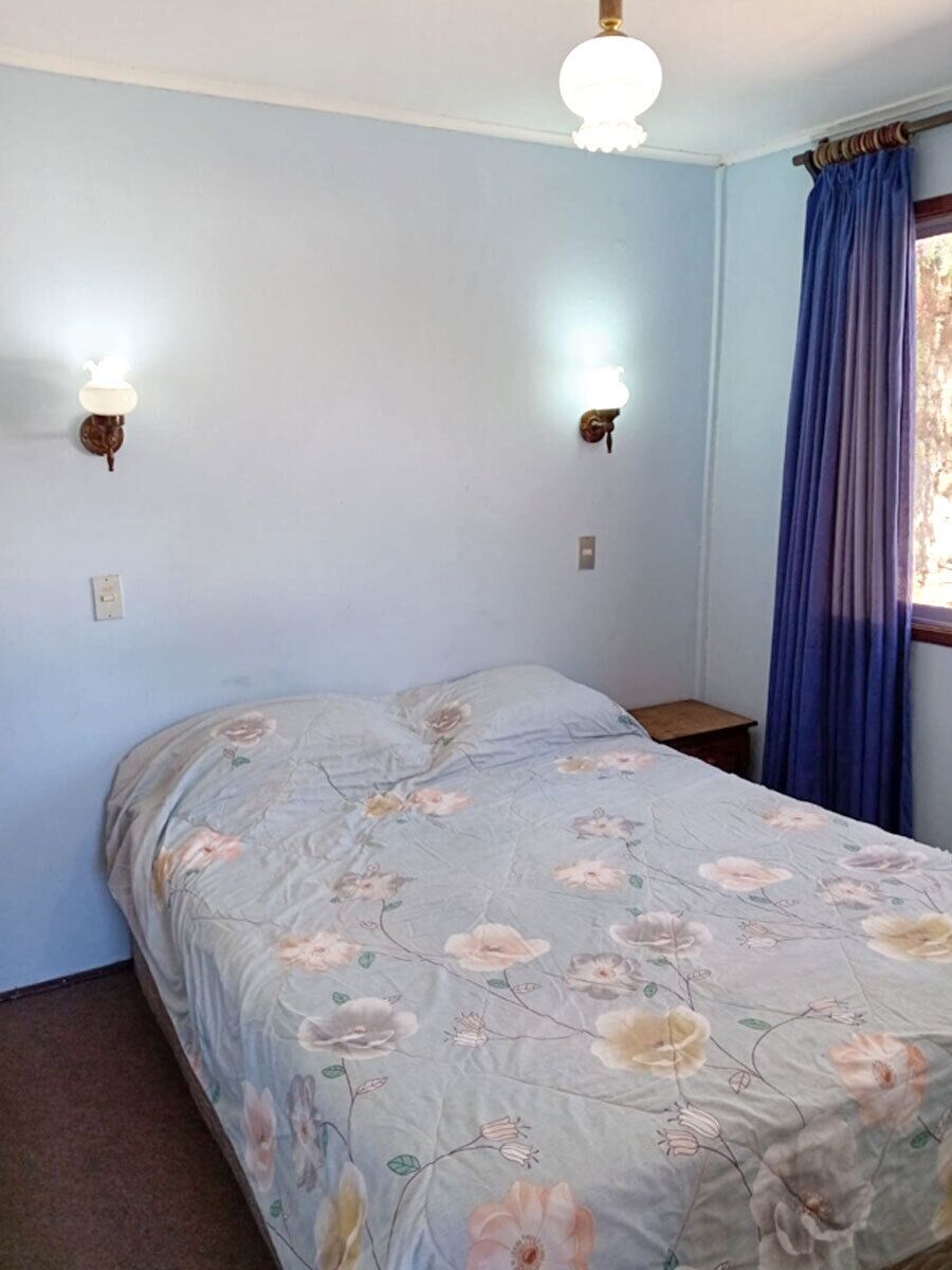 A bedroom with a bed, two wall-mounted lamps, a window with curtains, and a ceiling fan.