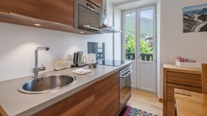 A modern kitchen with a stainless steel sink, wooden cabinets, a built-in oven, and a view of a mountainous landscape through a glass door. - 3P Apartment Chamonix, Close to Slopes, Pets Allowed, Parking, WiFi (Chamonix-Mont-Blanc)