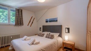 A bedroom with a bed, a bedside table, a nightstand, a radiator, a window with curtains, and a picture on the wall. - 3P Apartment Chamonix, Close to Slopes, Pets Allowed, Parking, WiFi (Chamonix-Mont-Blanc)