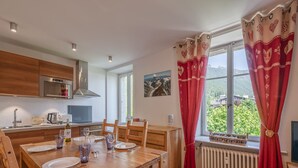A modern kitchen with wooden cabinets, a built-in oven, and a dining area with a wooden table set for four. - 3P Apartment Chamonix, Close to Slopes, Pets Allowed, Parking, WiFi (Chamonix-Mont-Blanc)