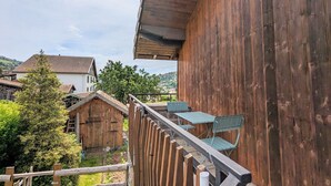 Un bâtiment en bois doté d’un balcon, d’une échelle et offrant une vue sur une maison et des arbres.