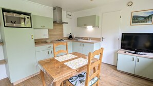 Une cuisine compacte équipée d’un four à micro-ondes, d’une cuisinière et d’un évier. On y trouve une table à manger avec des chaises, ainsi qu’un téléviseur posé sur un meuble.