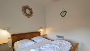 Un lit bien fait, avec du linge de lit blanc, dans une pièce dotée d’une tête de lit et d’un pied de lit en bois, de deux tables de chevet fixées au mur et d’un radiateur mural.
