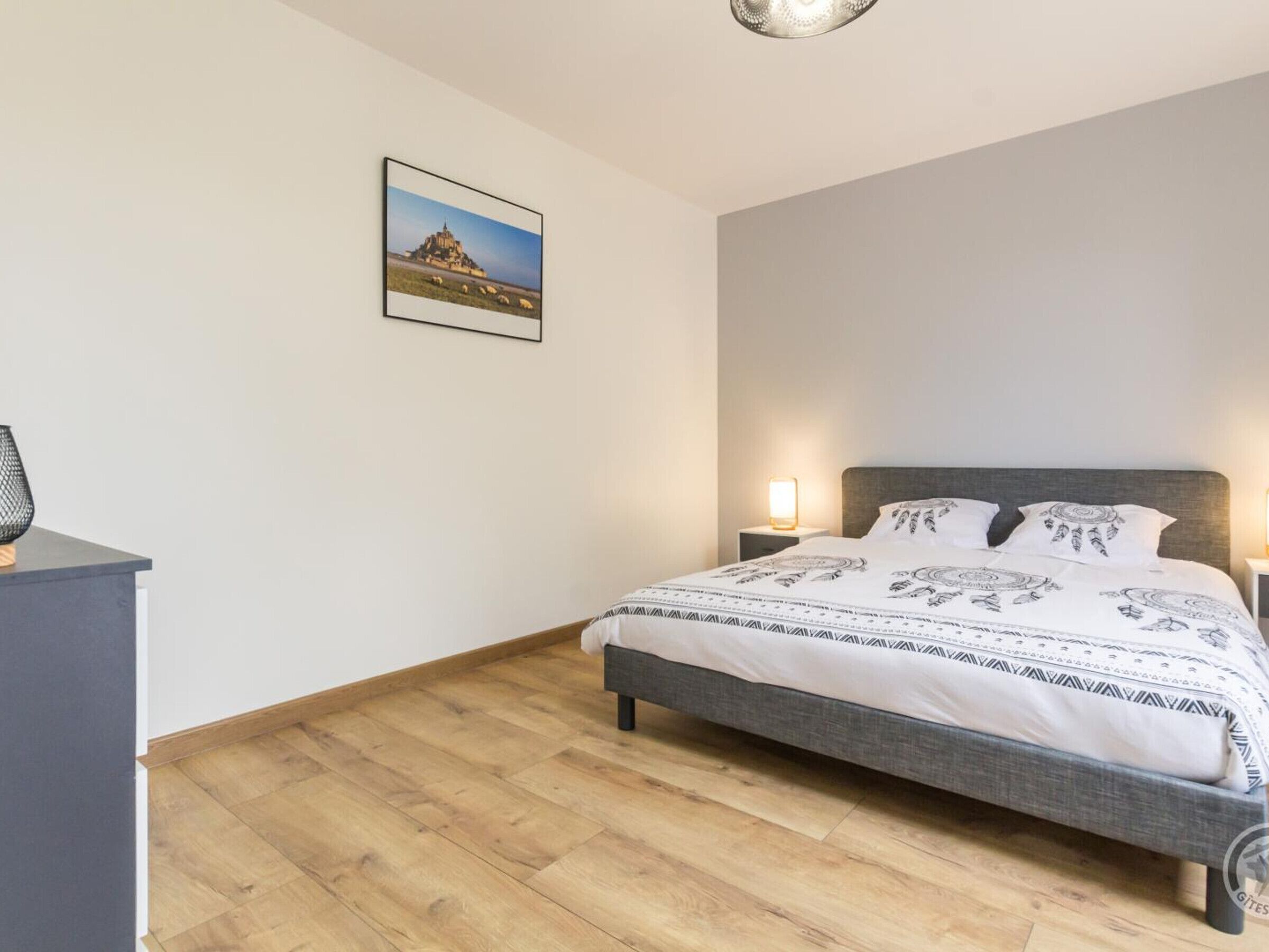 A neatly arranged bedroom with a bed, bedside lamps, a small table, and a picture on the wall.