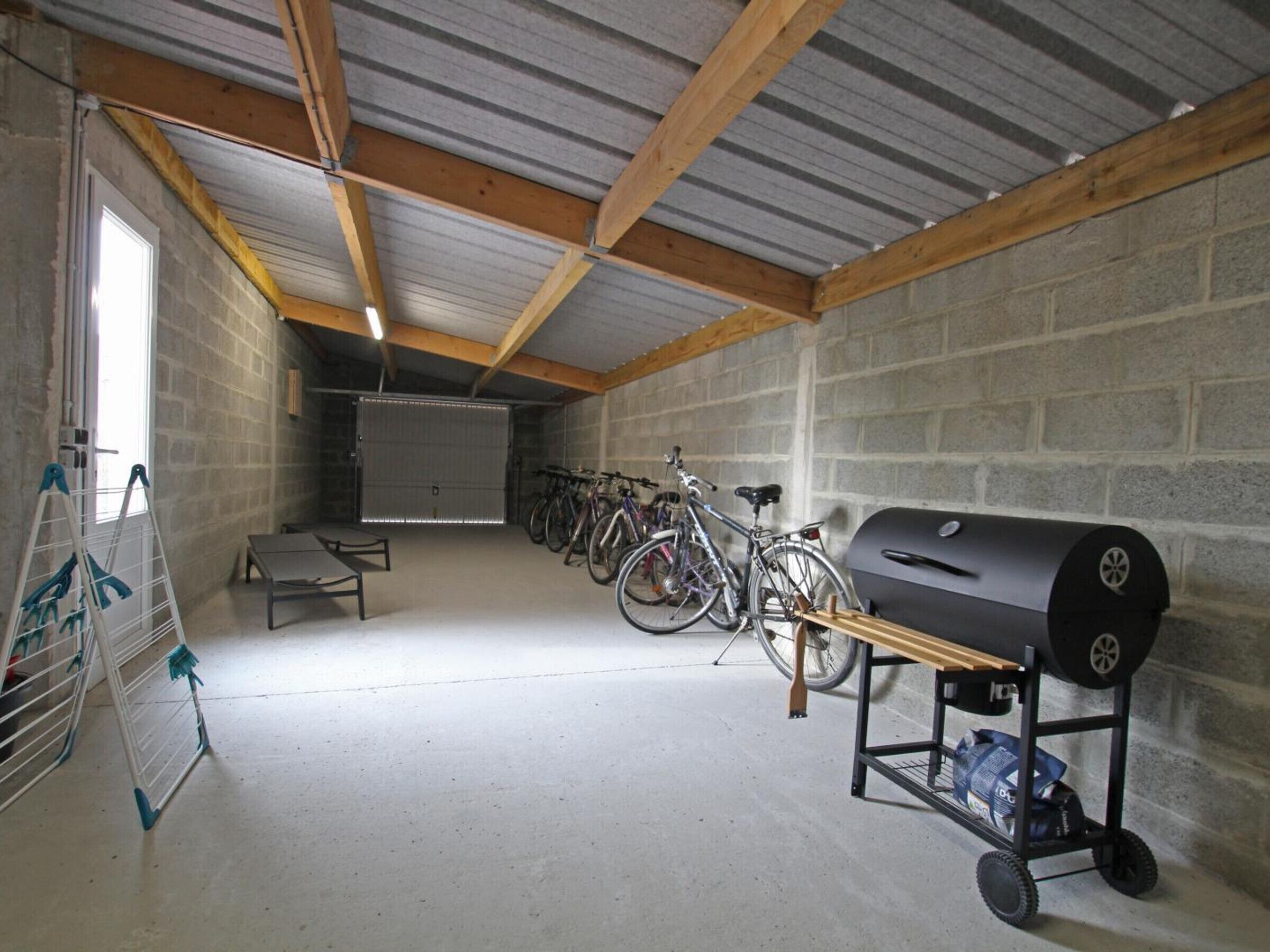 Un garage contenant des vélos, un barbecue et une table pliante.
