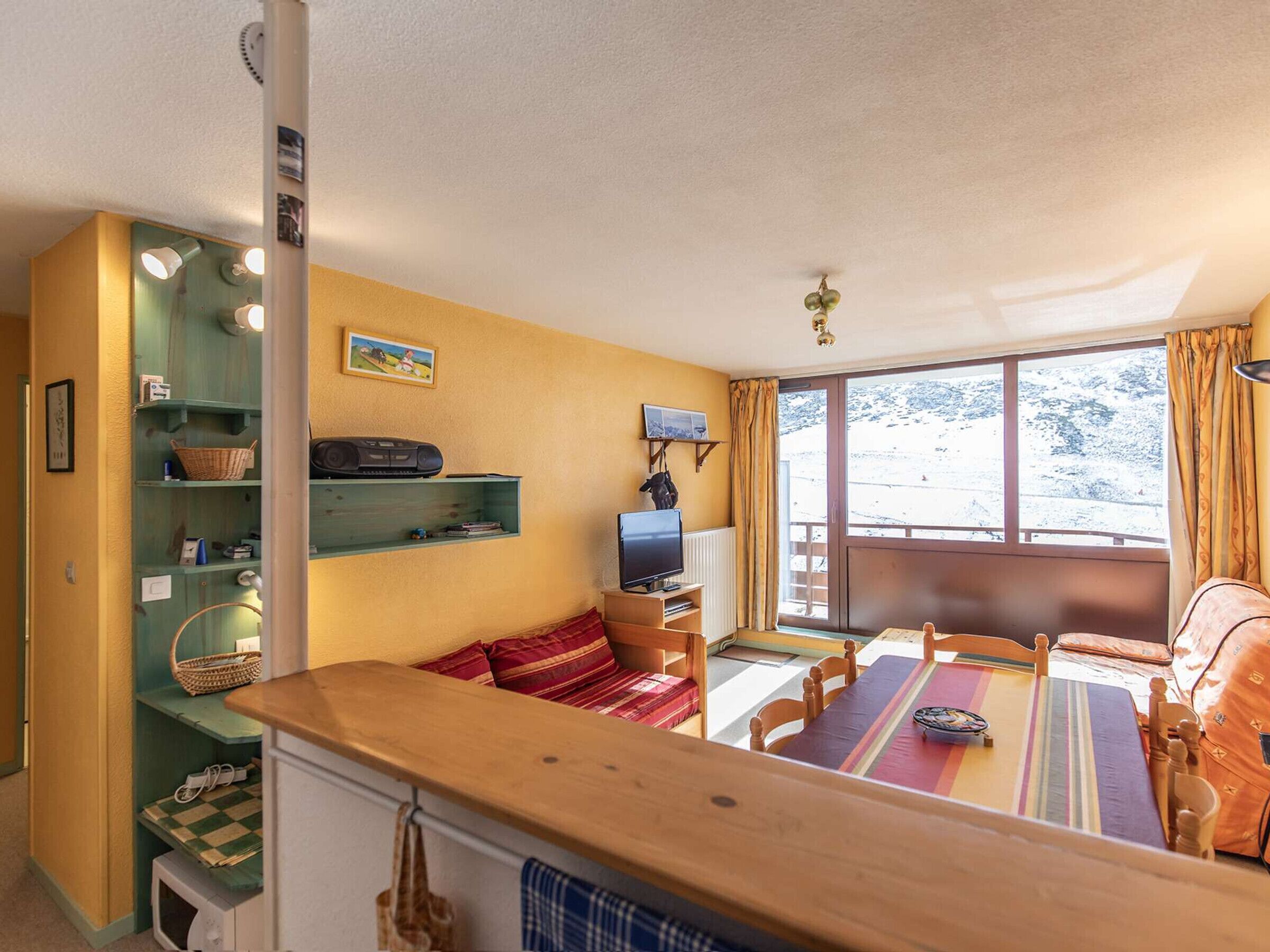Una sala de estar acogedora con una mesa de madera, un televisor y un ventanal que ofrece vistas a un paisaje nevado.