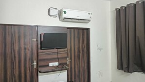 Une pièce avec un téléviseur fixé sur une porte en bois, un climatiseur au-dessus, et un rideau sur le côté droit.