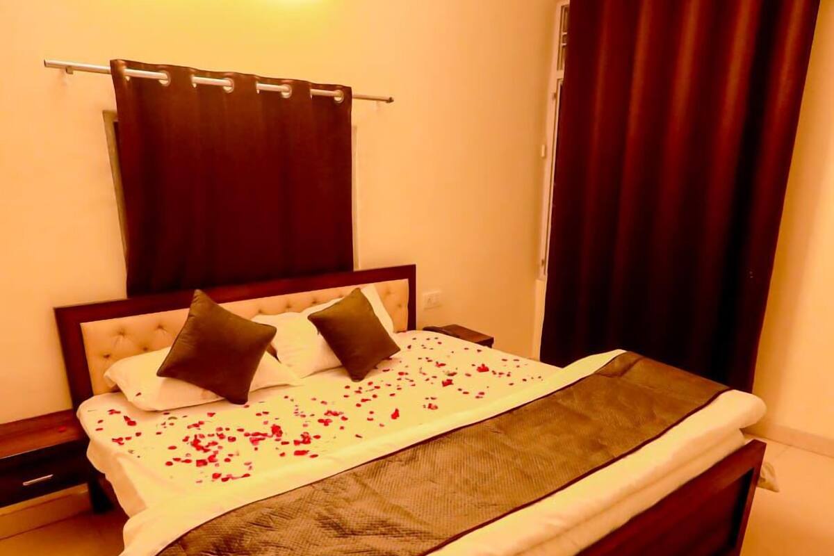 A neatly made bed with a white and brown bedspread, two pillows, and rose petals scattered on the bed.