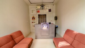 Un espace d’accueil d’hôtel comprenant un comptoir de réception, deux canapés, une horloge et un climatiseur fixé au mur.