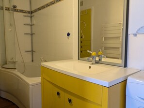 A bathroom with a bathtub, a sink with a mirror, and a yellow vanity. - 3-Bedroom Apartment at the Foot of Slopes - 8 pax (Le Dévoluy)