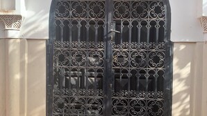 A black ornate gate with intricate designs, a stone bench in front, and a white wall with decorative elements.
