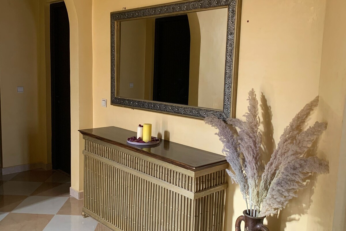 A reception area with a checkered floor, a wooden console table with a mirror above it, and a vase with dried flowers.