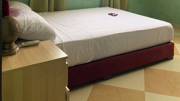 A room with a bed, a red chair, a window with curtains, and a wall with a decorative molding.