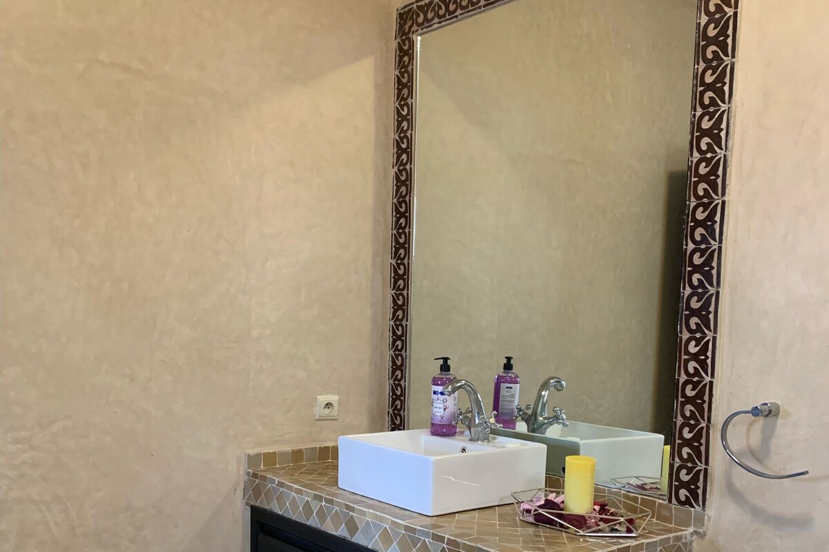 A bathroom with a tiled vanity, a mirror with a decorative frame, and two bottles of liquid soap.