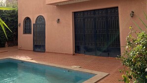 Un edificio de dos pisos con piscina, ventanas arqueadas y rejas metálicas decorativas.