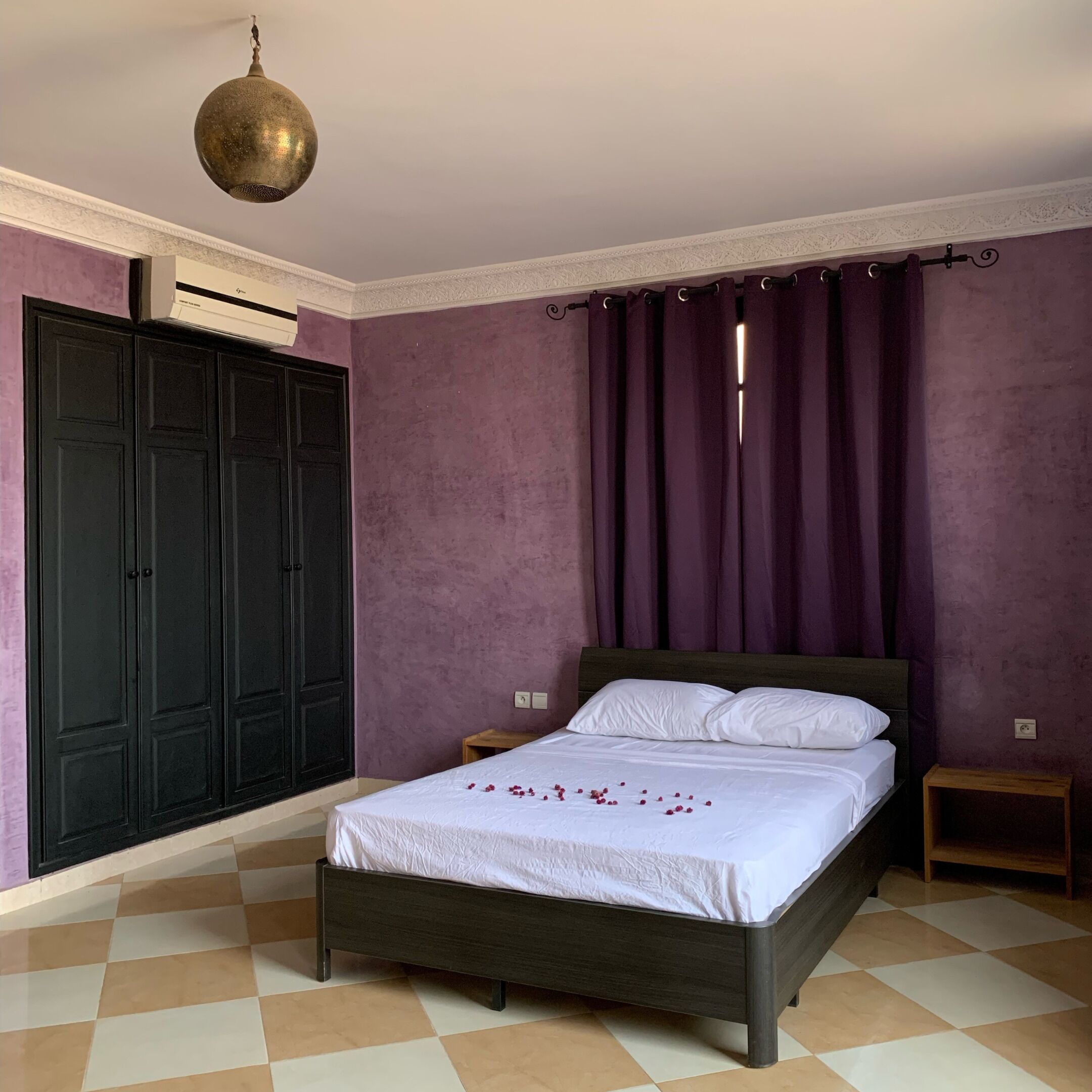 A bedroom with a bed, a wardrobe, a hanging light fixture, and a window with curtains.