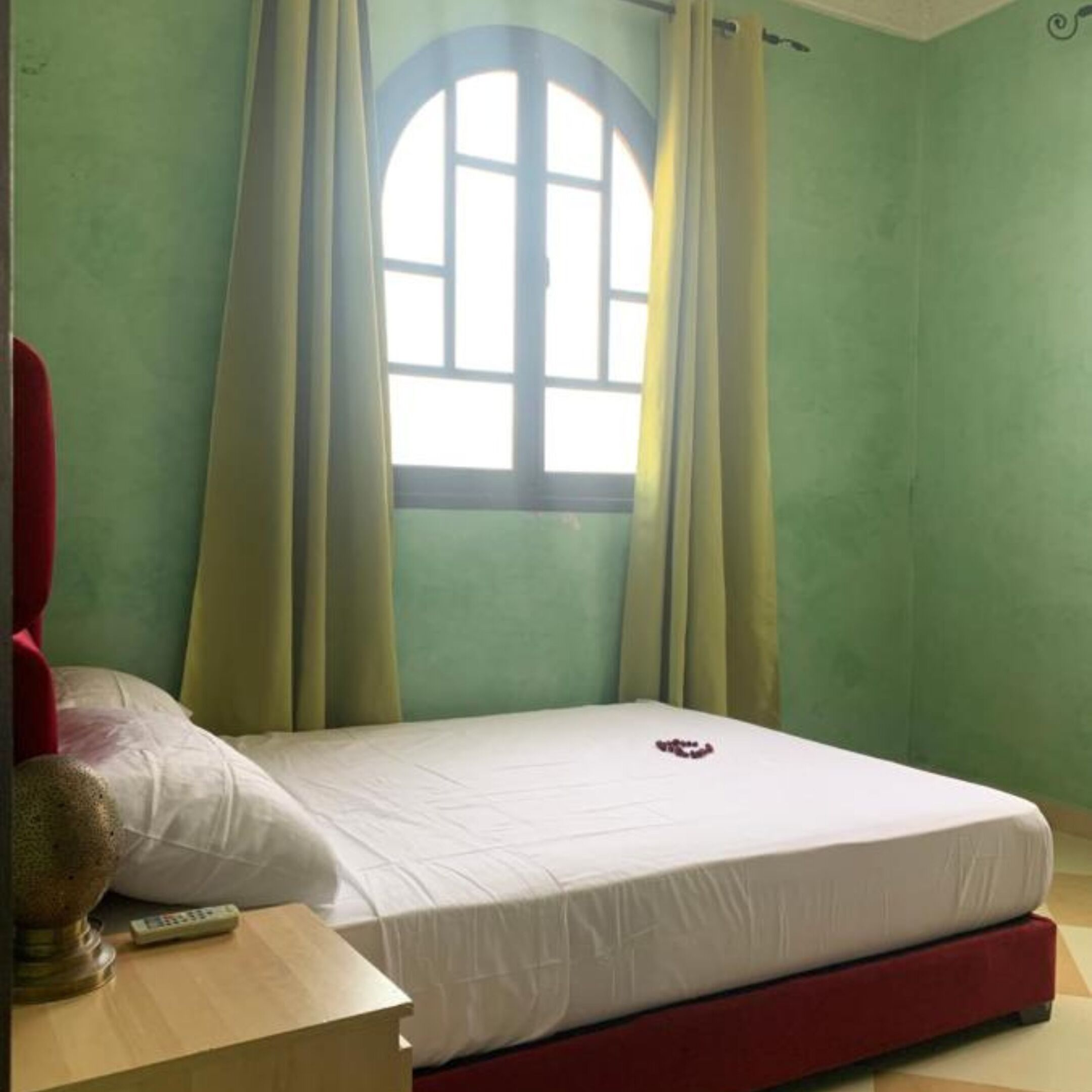 A room with a bed, a nightstand, a lamp, and a window with curtains.