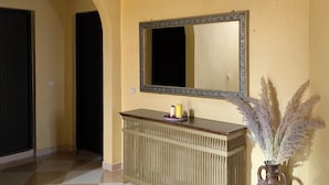 Un pasillo con piso a cuadros, techo de madera, un espejo en la pared, una consola con velas y un jarrón con flores secas.