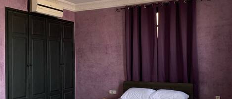 A bedroom with a bed, a wardrobe, a ceiling fan, and a window with purple curtains.
