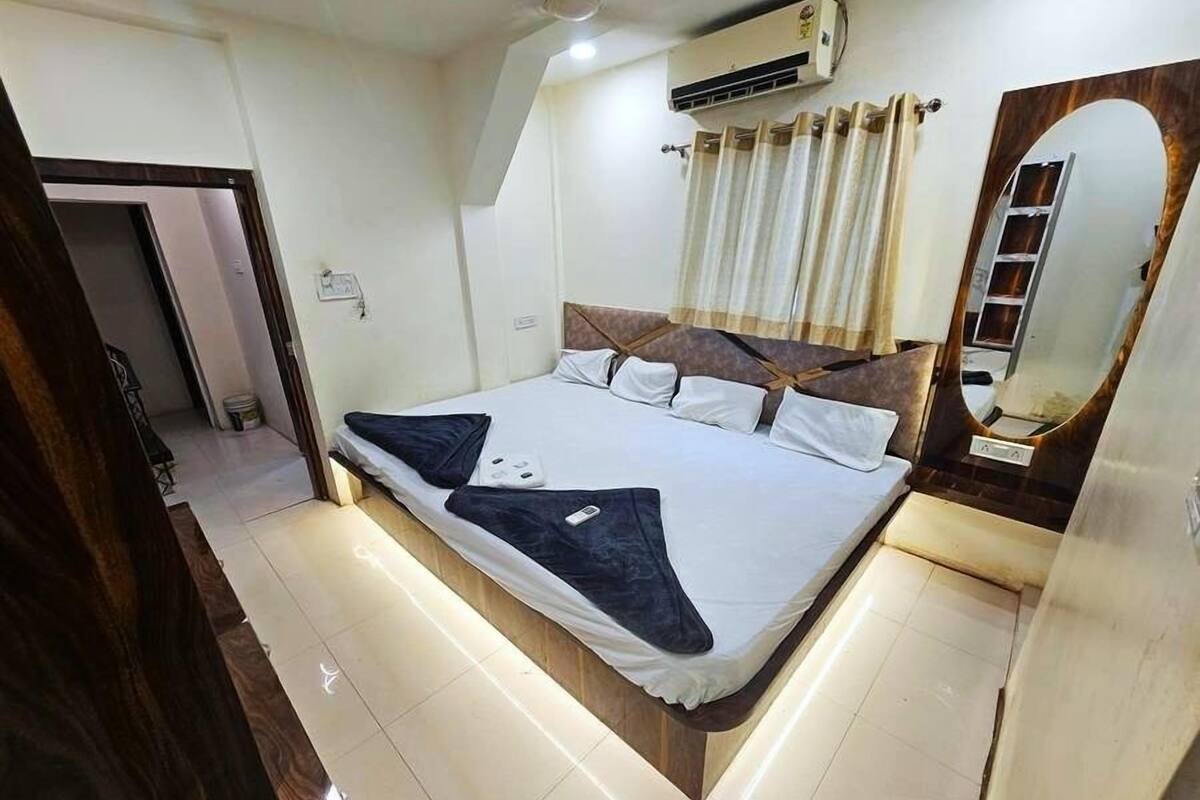 A modern hotel room with a large bed, a built-in wardrobe, a mirror, and an air conditioning unit.