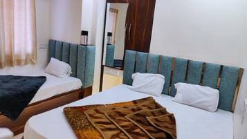 A hotel room with two beds, each with a headboard and pillows. There is a mirror on the wall and a window with curtains.