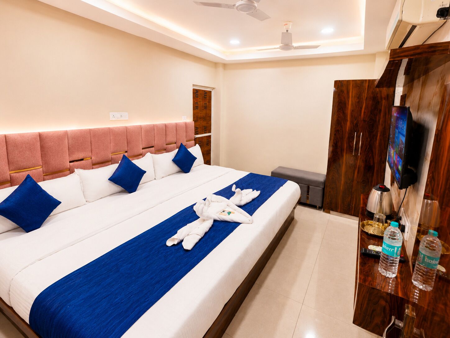 A hotel room with a large bed, a wooden wardrobe, a television, and a minibar.