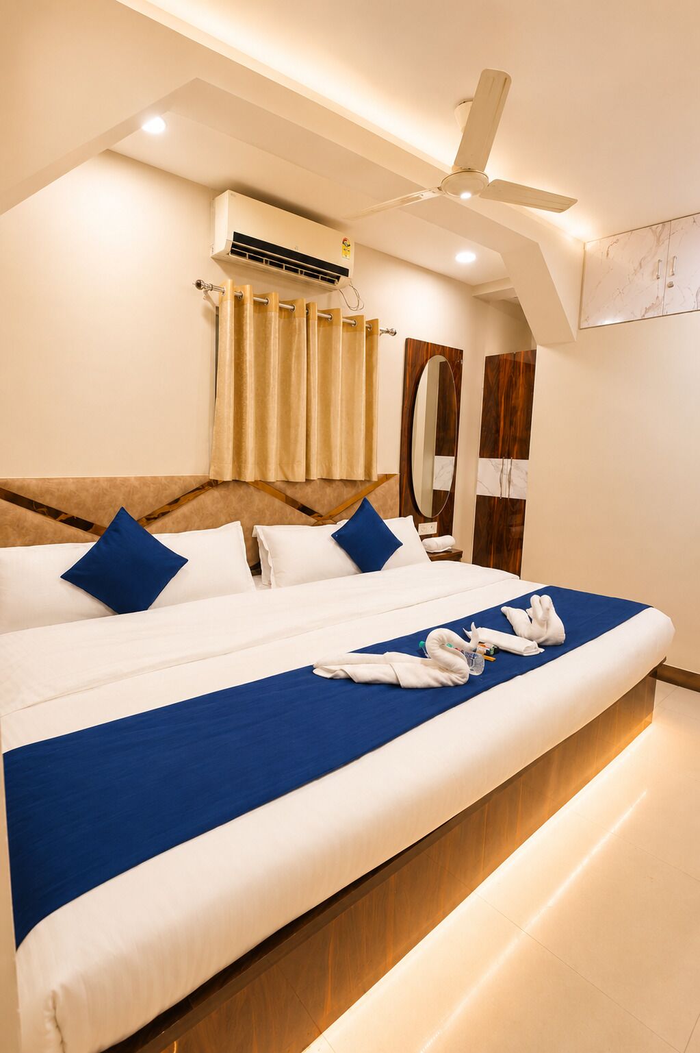 A hotel room with a large bed, a ceiling fan, an air conditioning unit, and a wooden headboard.