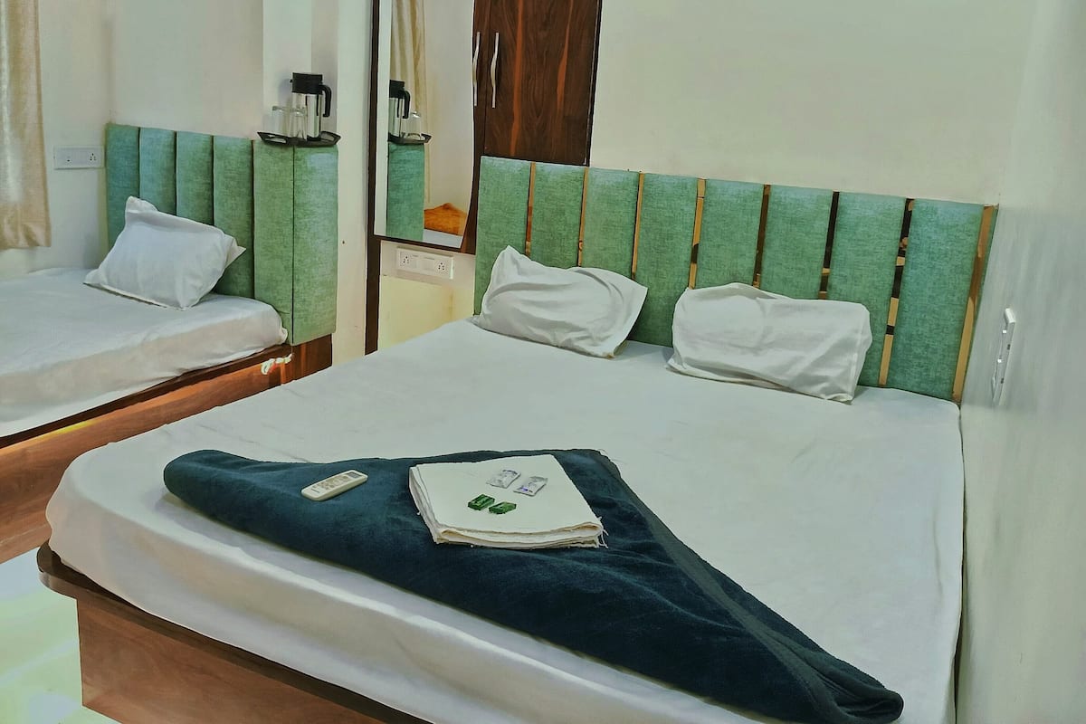A hotel room with two beds, each with white bedding and green headboards. There is a mirror on the wall, a small table with a kettle, and a window with curtains.
