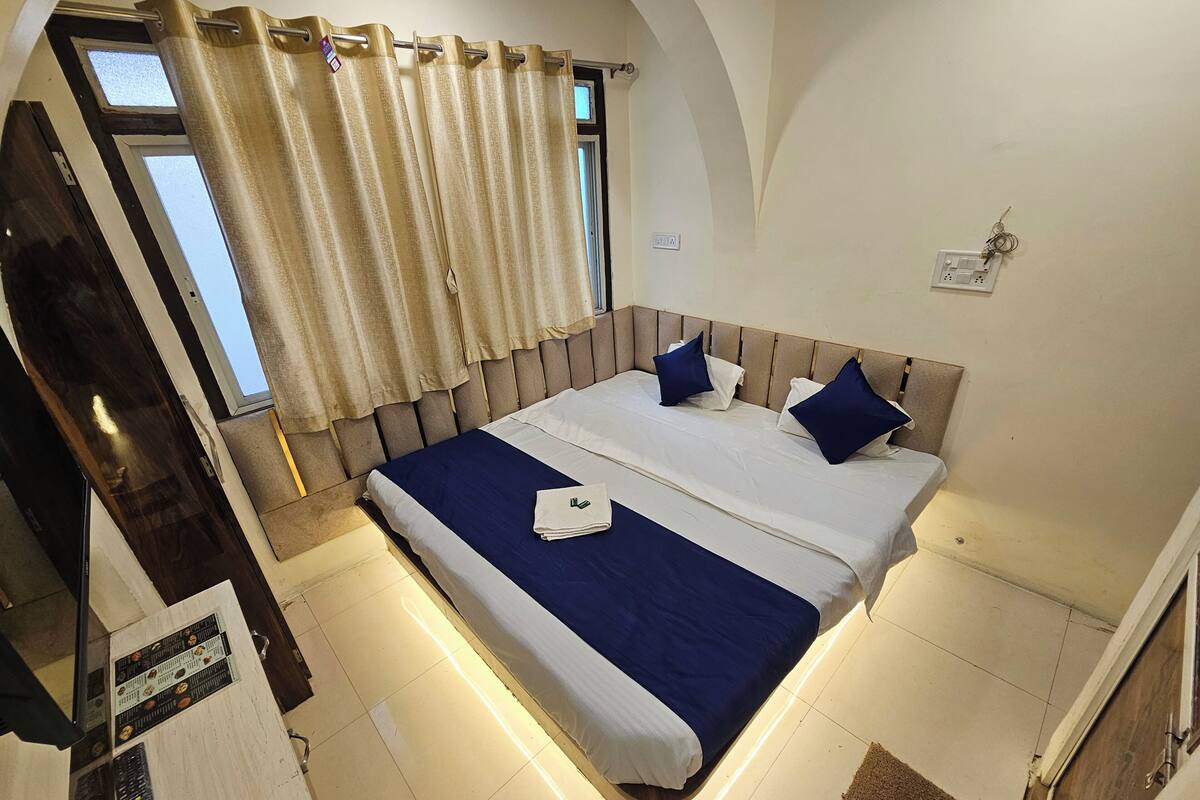 A hotel room with a large bed, a window with curtains, a headboard, and a tiled floor.