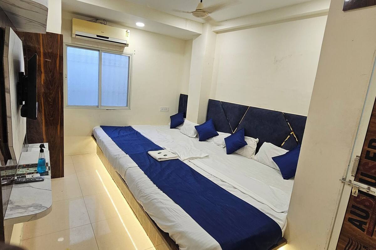 A bedroom with a bed, a window, an air conditioning unit, and a door with a wooden panel.