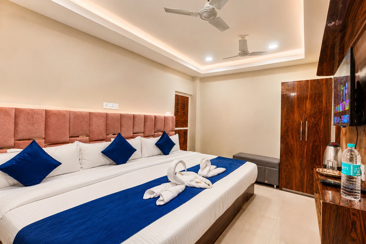 A hotel room with a large bed, a wooden wardrobe, a television, and a ceiling fan.