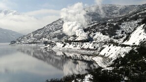 Um trem em uma linha de trem coberta por neve, com um lago ao primeiro plano.