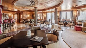 A spacious dining area with multiple tables and chairs, a central column, and a ceiling with a decorative design. - HOTIDAY Room Collection - Campiglio Pradalago (Pinzolo)