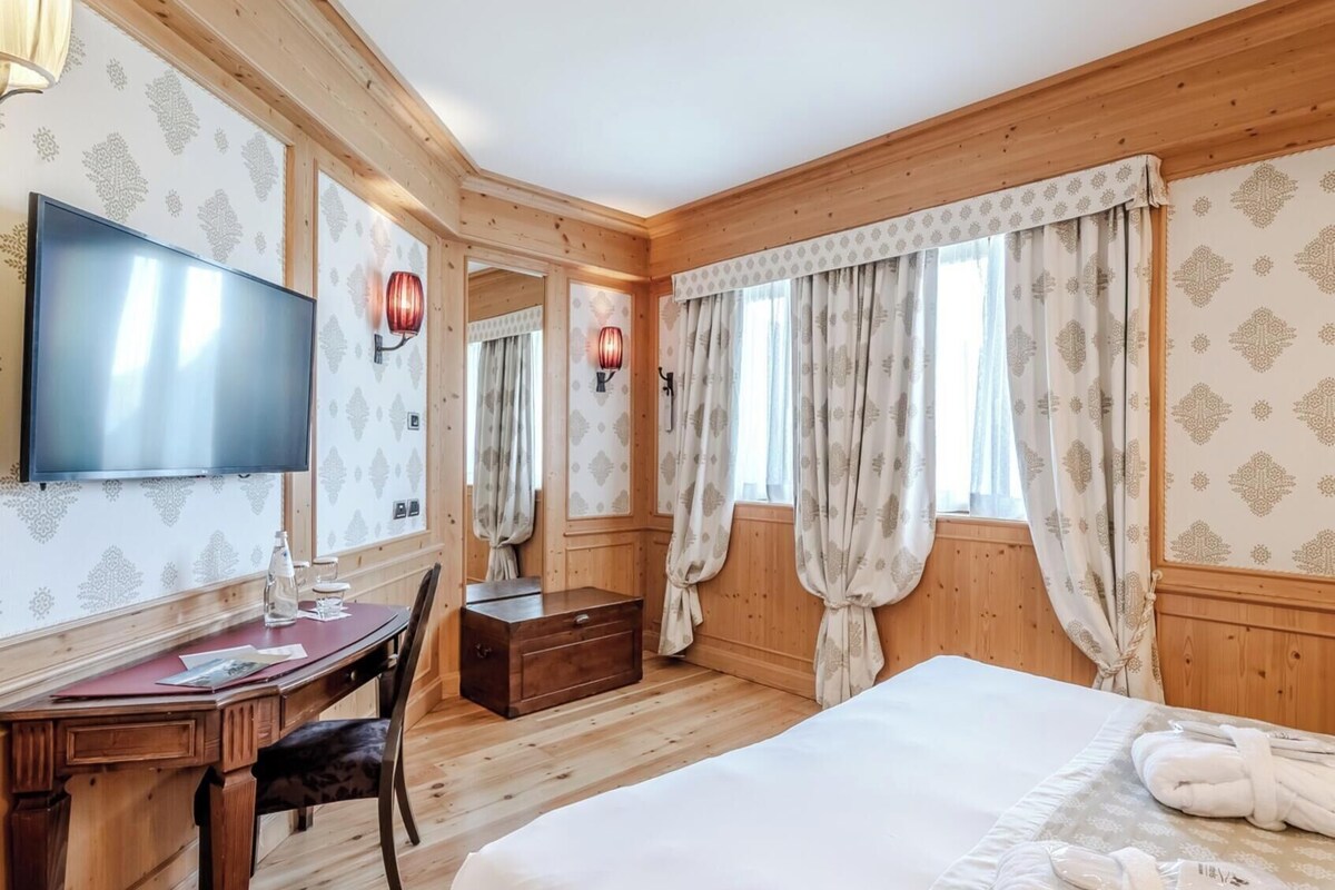 Een hotelkamer met houten lambrisering, een flatscreen televisie, een bureau met stoel, een bed met wit beddengoed en een badkamer met douchegordijn.