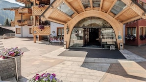A wooden building with a large arched entrance, balconies with flower boxes, and a paved courtyard. - HOTIDAY Room Collection - Campiglio Pradalago (Pinzolo)