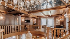 A grand interior with a wooden staircase, ornate chandeliers, and a television mounted on a wooden panel. - HOTIDAY Room Collection - Campiglio Pradalago (Pinzolo)