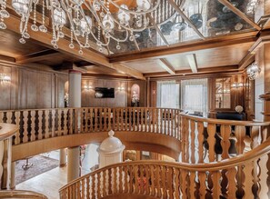 Een luxueus interieur met een statige trap, houten lambrisering en versierde kroonluchters.