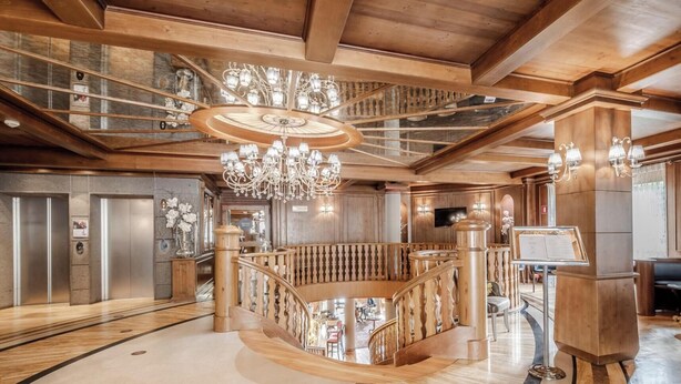 A grand lobby with a central wooden staircase, a chandelier, and a reception desk. - HOTIDAY Room Collection - Campiglio Pradalago (Pinzolo)