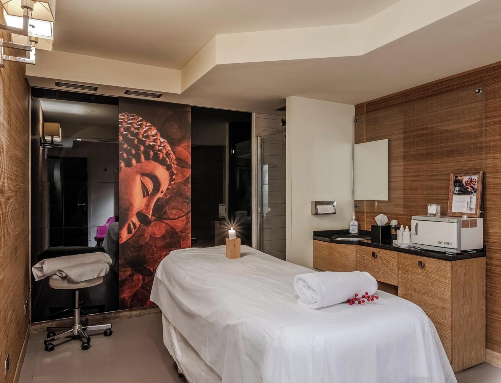 Habitación de hotel con cama, tocador de madera, calentador de toallas y una pared con un mural de Buda.