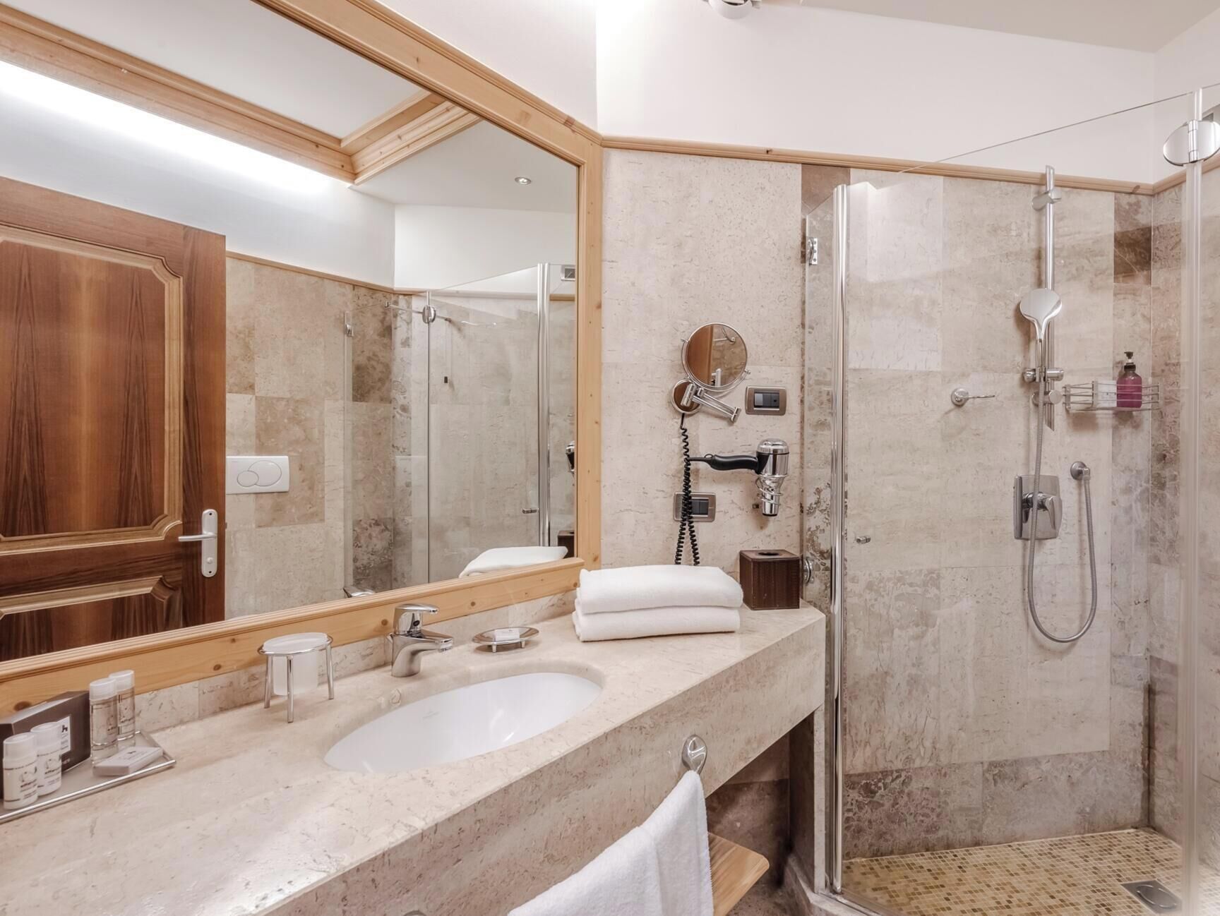 A bathroom with a large mirror, a sink, a shower, and a towel rack.