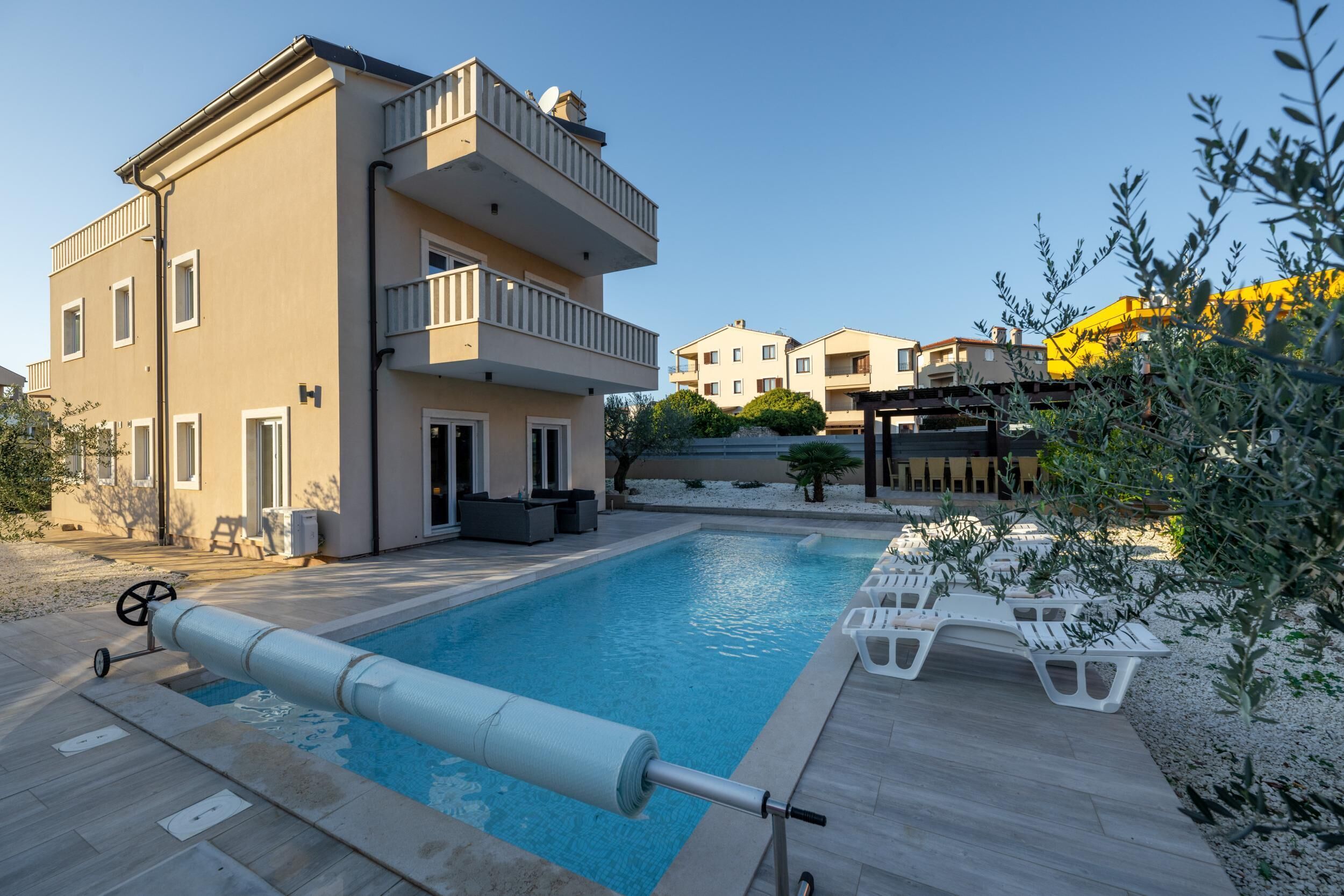 A swimming pool with a retractable cover, surrounded by outdoor seating and a multi-story building with balconies.
