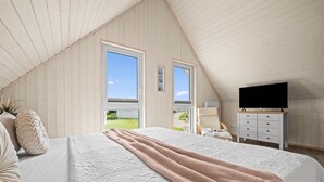 Une chambre dotée d’un grand lit, d’une télévision et offrant une vue sur un paysage verdoyant par les fenêtres.