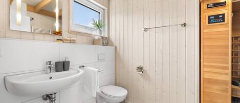 A modern bathroom with a white sink, toilet, and wooden panel walls.