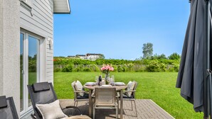 Une terrasse avec une table dressée pour le repas, des chaises d’extérieur et une vue sur une maison en arrière-plan.